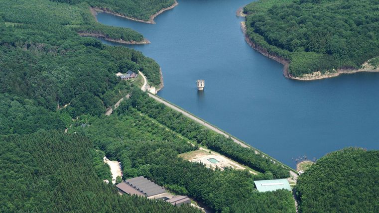 Een schilderachtig meer omgeven door groene bossen. In het midden is een kleine pier zichtbaar.