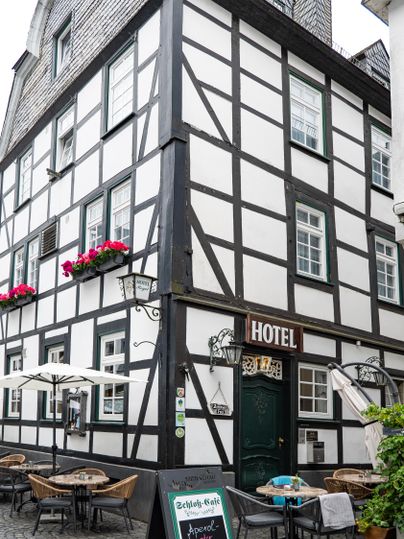 A traditional half-timbered house with the inscription "HOTEL". Outside, there are tables and chairs with parasols.