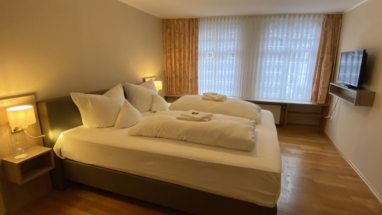 A bright hotel room with two beds and large windows. There are modern furnishings and soft lighting.