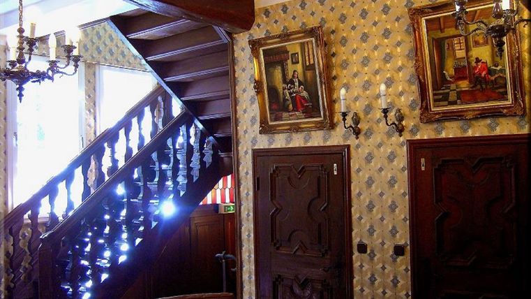 Ein klassischer Flur mit einer Holztreppe und dekorativen Wänden. An den Wänden hängen Bilder und es gibt elegante Wandlampen.