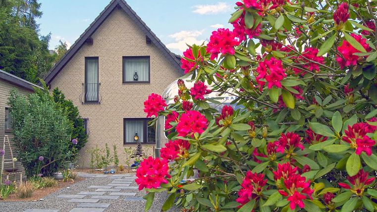 Ein schönes Haus umgeben von bunten Rhododendren. Der Garten ist gut gepflegt und der Himmel ist klar.