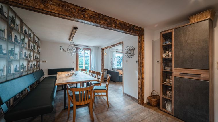 Een moderne eetkamer met een grote houten tafel en houten stoelen. Aan de muur zijn foto's tentoongesteld, en een koelkast staat in de hoek.