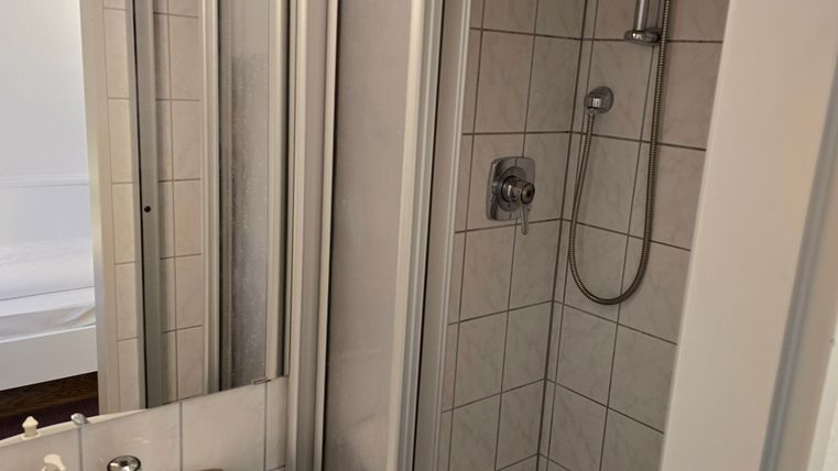 A modern bathroom with a shower and a sink. The walls are tiled and there is a mirror.