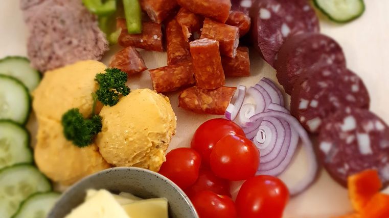 A colorful plate with various slices of cold cuts and cheese, fresh vegetables, and dip. The ingredients are beautifully arranged and invite you to enjoy.