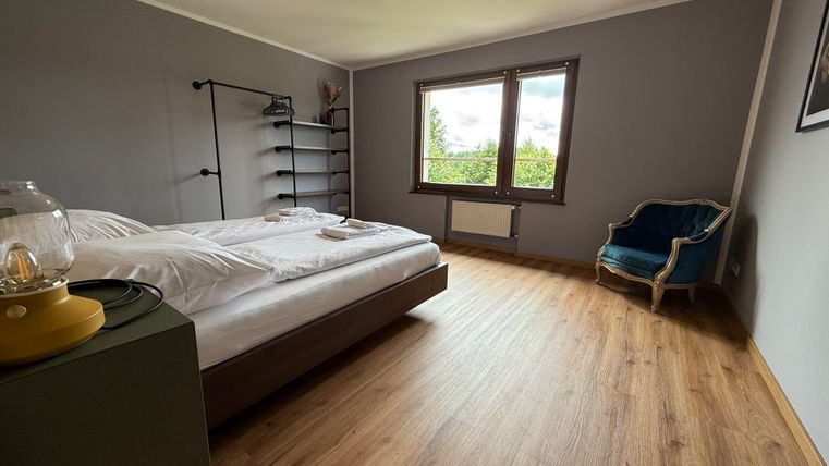 Een moderne slaapkamer met een tweepersoonsbed en grote ramen. De ruimte heeft een houten vloer en een gezellige zitgelegenheid in de hoek.