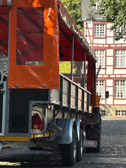 Een oranje hanger staat op een geplaveide straat. Op de achtergrond zijn historische gebouwen te zien.