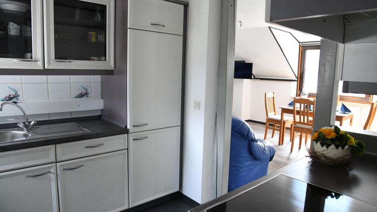 A modern kitchen with white cabinets and stainless steel appliances. In the background, there is a cozy living area with a table and chairs.