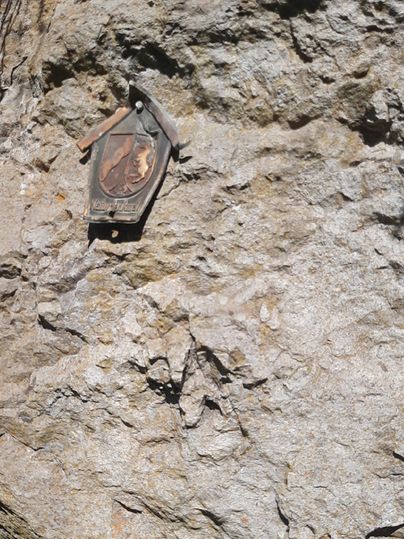 Ein bronzefarbenes Schild ist an einer Felswand befestigt. Der Hintergrund besteht aus rauem, grauem Gestein.