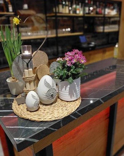 A beautiful decoration on a bar with Easter eggs, flowers, and a candle. The table has a modern aesthetic with an elegant marble pattern.