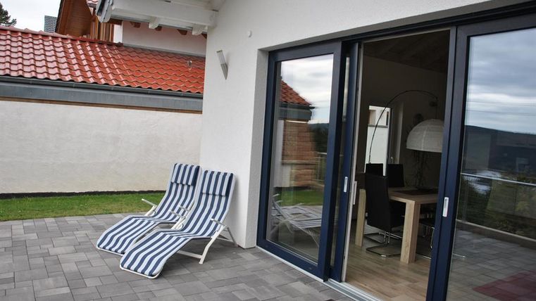 Een zonnig terras met twee ligstoelen en uitzicht op de woonkamer. De omgeving is rustig en uitnodigend.