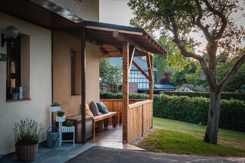 Een gezellige buitenruimte met een houten veranda en een bank. Op de achtergrond zijn een onderhouden tuin en enkele bomen zichtbaar.