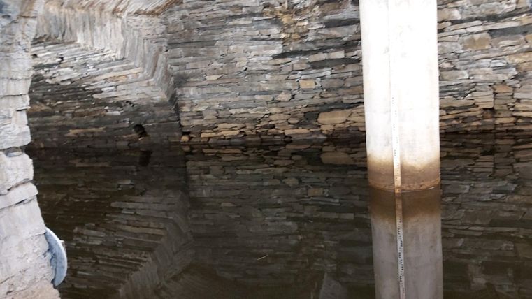 Een ondergrondse ruimte met stenen muren en een wateroppervlak. Een kolom staat in het midden en wordt weerspiegeld in het water.