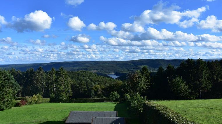 A picturesque landscape with green meadows and trees. The sky is blue, and white clouds are floating above.