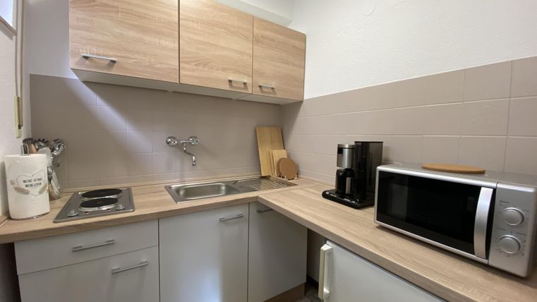 A modern kitchen with bright wooden cabinets and a practical layout. It includes a stove, a faucet, a coffee machine, and a microwave.
