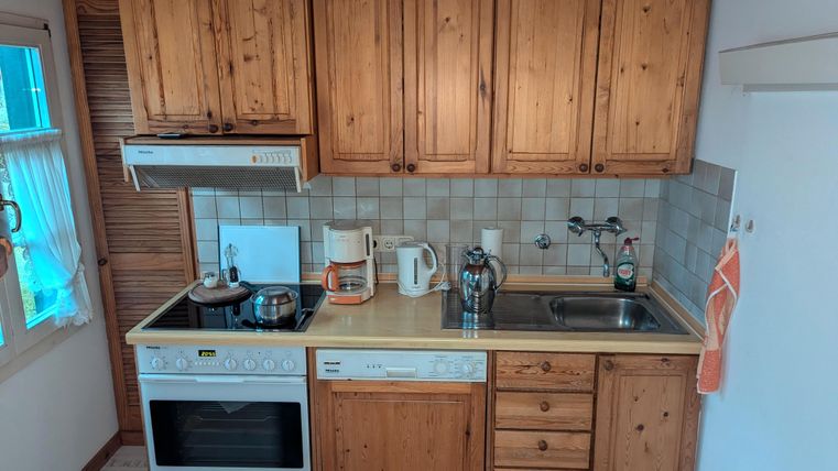 A cozy kitchen with wooden cabinets and modern appliances. The room is bright and features a practical layout of stove, sink, and work surface.