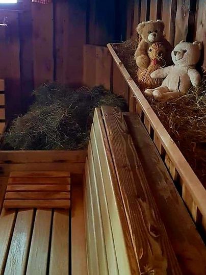 A cozy room with wooden paneling, where two fabric bears sit on a wooden shelf next to hay. The atmosphere feels warm and inviting.