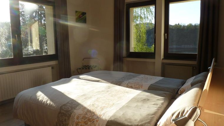 A bright bedroom with a large double bed and large windows. The light gently falls on the bed linen and the room.