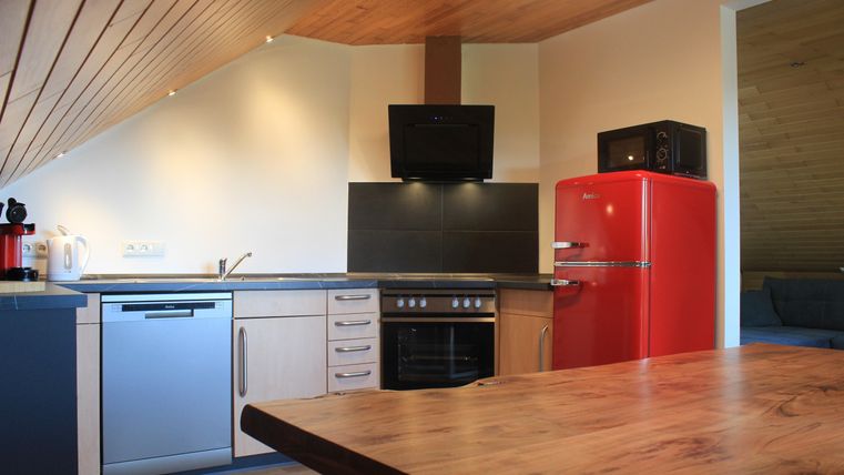 A modern kitchen with a wooden ceiling and appliances in elegant colors. The red refrigerator is a striking eye-catcher.