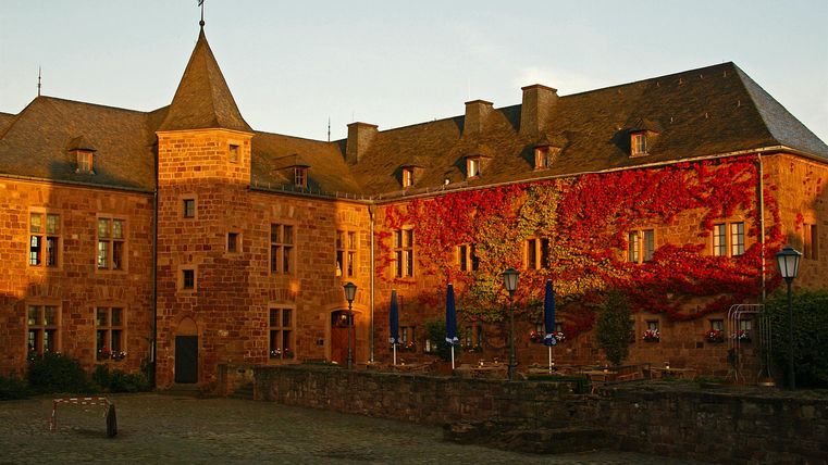 Een historisch kasteel met een kenmerkende toren en een kleurrijke muurschildering. Het gebouw is omgeven door zacht licht en straalt een uitnodigende sfeer uit.