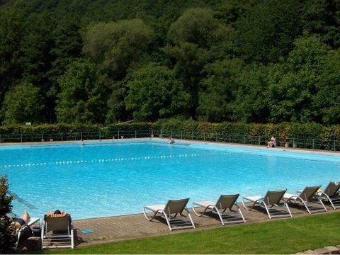 Ein großes Schwimmbecken mit klarem, blauem Wasser. Umgeben von üppigem Grün und Liegen zum Entspannen.