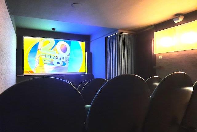A small movie theater with rows of black chairs. A colorful image is displayed on the screen.