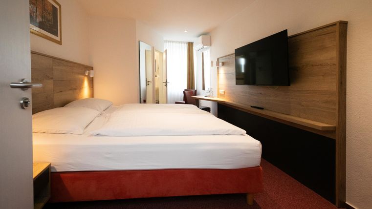 Ein modernes Hotelzimmer mit einem großen Doppelbett und einem Flachbildfernseher. Der Raum ist hell und freundlich gestaltet.