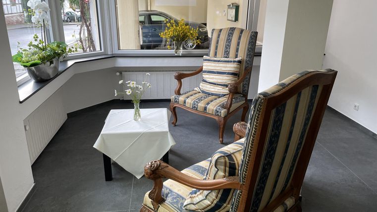 A cozy room with two chairs and a small table. Plants are at the window, and the room has plenty of daylight.