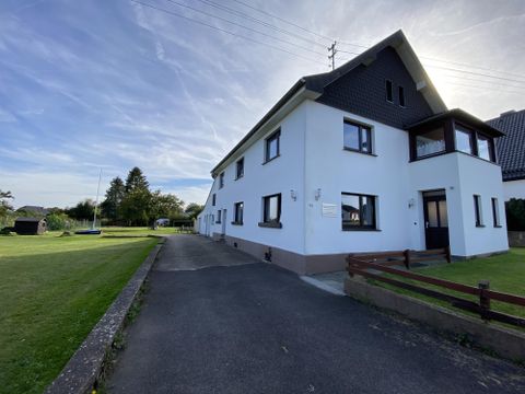 Een moderne, witte woning met meerdere vensters en een groen buitenterrein. De lucht is helder en er is een geasfalteerde oprit.