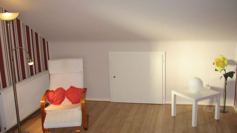 Een gezellige kamer met een witte fauteuil en een kleine tafel. Aan de wand zijn gestreepte behang en een lamp zorgt voor licht.