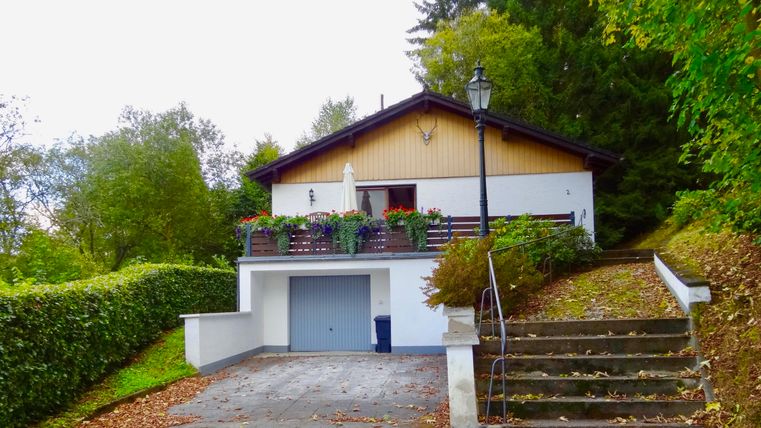 Ein schönes Haus in einer grünen Umgebung mit einem gepflegten Garten. Die Terrasse ist mit Blumen dekoriert, und eine Treppe führt zur Haustür.