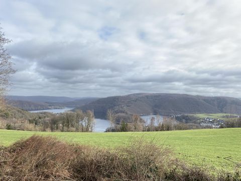 A picturesque landscape with gentle hills and a tranquil lake. The sky is cloudy, but the green meadow exudes freshness.