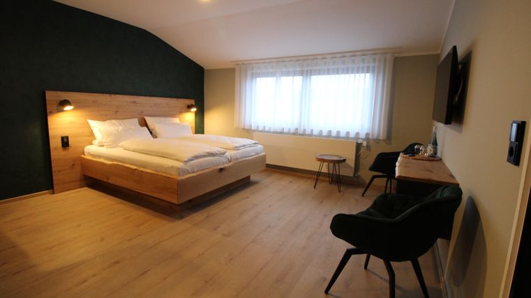 A modern bedroom with a large bed and stylish furniture. The windows let in plenty of daylight and create a pleasant atmosphere.