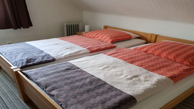 Een gezellige kamer met twee eenpersoonsbedden. Het beddengoed is in warme kleuren en zorgt voor een uitnodigende sfeer.