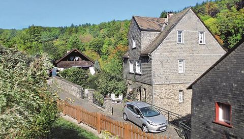 Ein charmantes Haus aus Stein mit einem schönen Garten und einem kleinen Parkplatz. Im Hintergrund sind Bäume und eine ruhige Landschaft zu sehen.