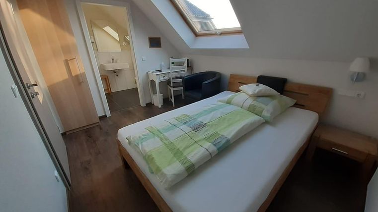 Ein gemütliches Zimmer mit einem Doppelbett und einem großen Fenster. Es gibt einen kleinen Schreibtisch und einen Stuhl in der Ecke.