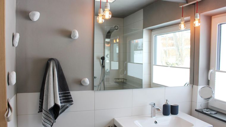 A modern bathroom with a white sink, a large mirror, and stylish lamps. The walls are bright, and the room is well-lit with natural light.
