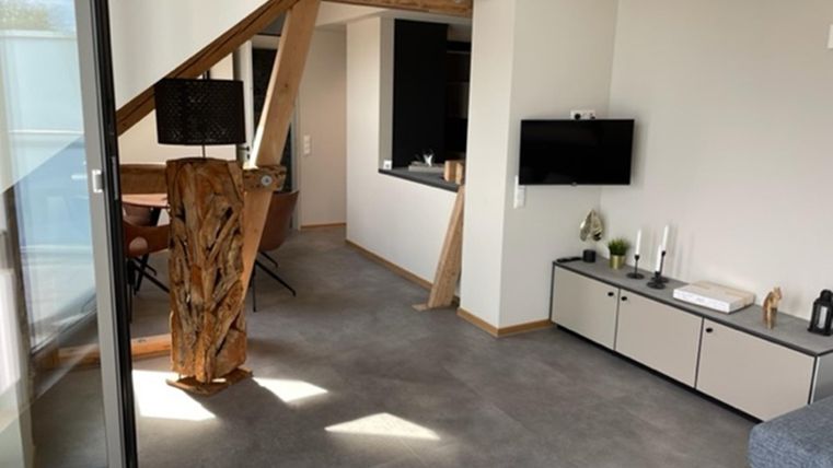 Een moderne woonkamer met houten details en een open ruimteconcept. De inrichting is eenvoudig en functioneel, met een televisie en een comfortabele stoel.
