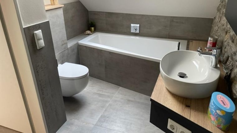 Een moderne badkamer met een bad, een toilet en een wastafel. De muren zijn in neutrale kleuren gehouden, en er is een dakraam voor natuurlijk licht.