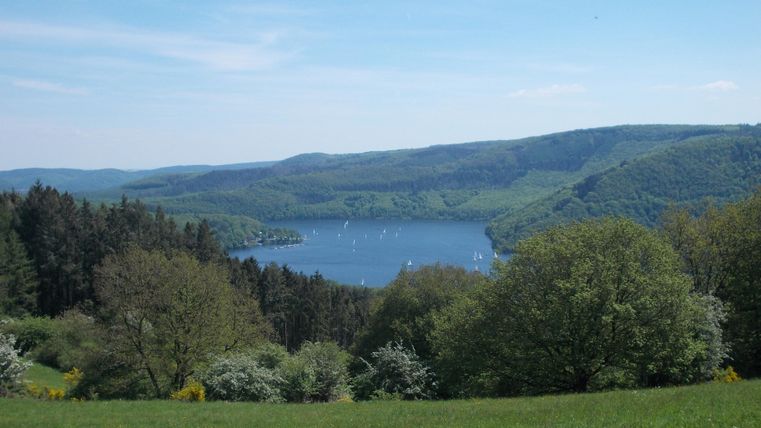 Een schilderachtig meer omringd door groene heuvels en bomen. De lucht is helder en blauw, ideaal voor buitensportactiviteiten.