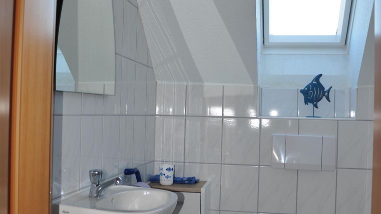 A modern bathroom with white tiles and a small window. There is a sink and a toilet, as well as a few decorative elements.