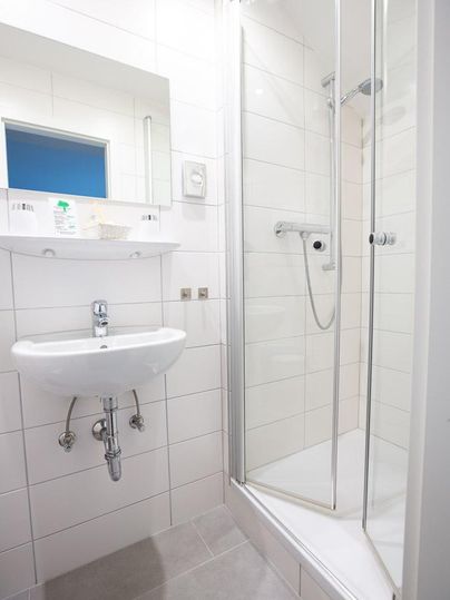 A modern bathroom with a shower and a sink. The walls are brightly tiled, and there is a mirror above the sink.