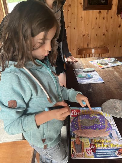 Een kind tekent met een pen op een tijdschrift. Op de achtergrond zijn er meer tijdschriften en een houten tafel te zien.