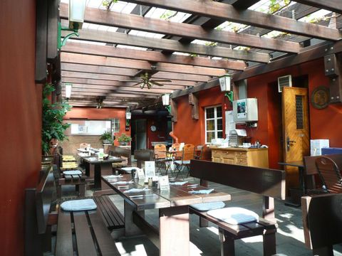 Een uitnodigende buitenruimte van een restaurant met houten meubels en begroeide muren. De zonneschijn zorgt voor een vriendelijke sfeer.