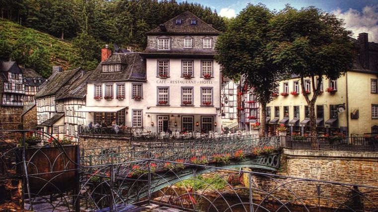 A picturesque inn with traditional architecture stands by a small river. Surrounded by trees and hills, the place invites you to linger.