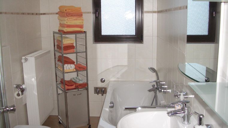 A modern bathroom with a bathtub, a sink, and a toilet. Several towels are neatly stacked on a shelf.