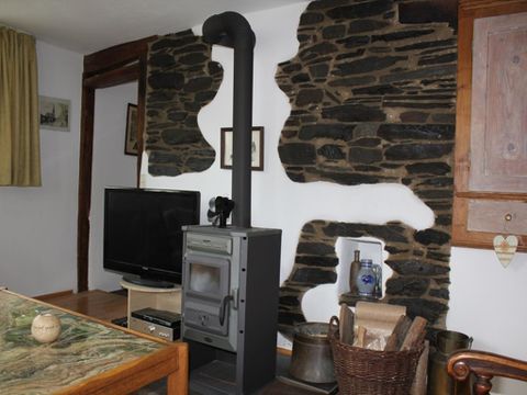 A cozy living room with a wood stove and a stone wall. In the background, there is a television and there are rustic furniture.