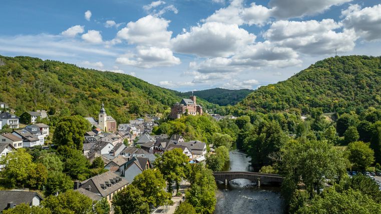 A picturesque valley with a small town by the river. Green hills surround the gentle landscape under a clear sky.