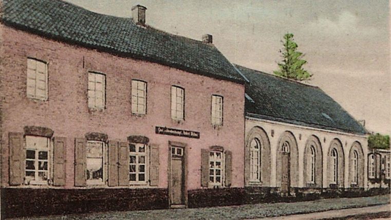 An old, charming building with a pink facade and many windows. Next to it stands another annex with round windows and a dark roof.