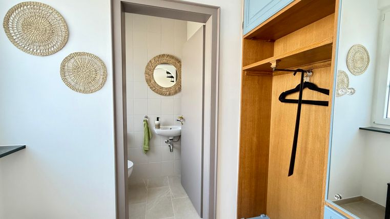 Een lichte entree met een garderobe en een spiegel. Aan de muur hangen decoratieve wandplanken.