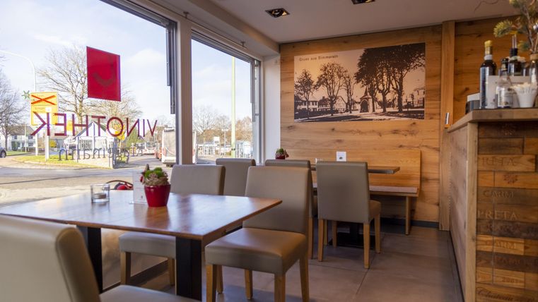 A cozy café with wooden furniture and large windows. Through the windows, a pleasant light atmosphere can be seen.